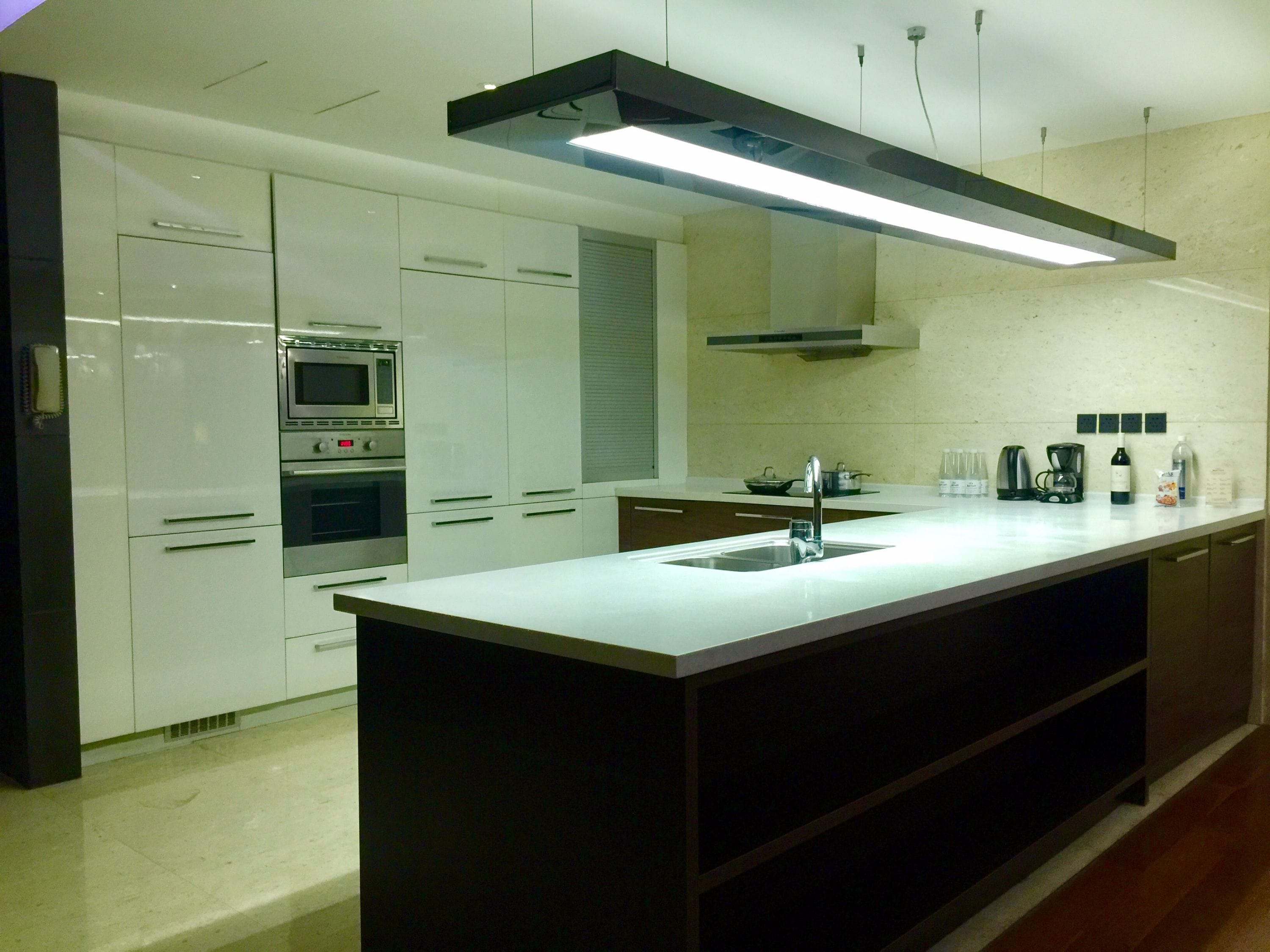 Een moderne keuken met witte kasten, een centraal eiland, roestvrijstalen apparatuur en een lineaire verlichtingsarmatuur.