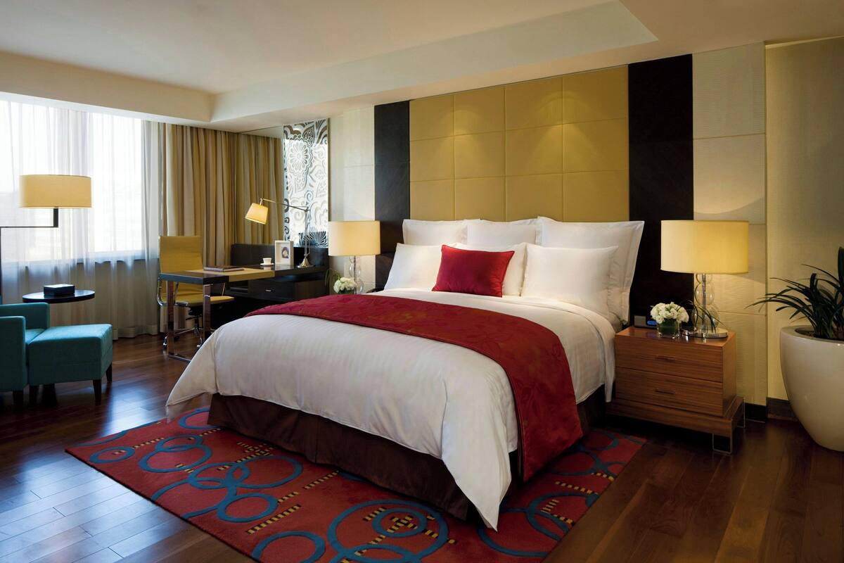 A hotel room with a large bed, a desk, a chair, and a potted plant.