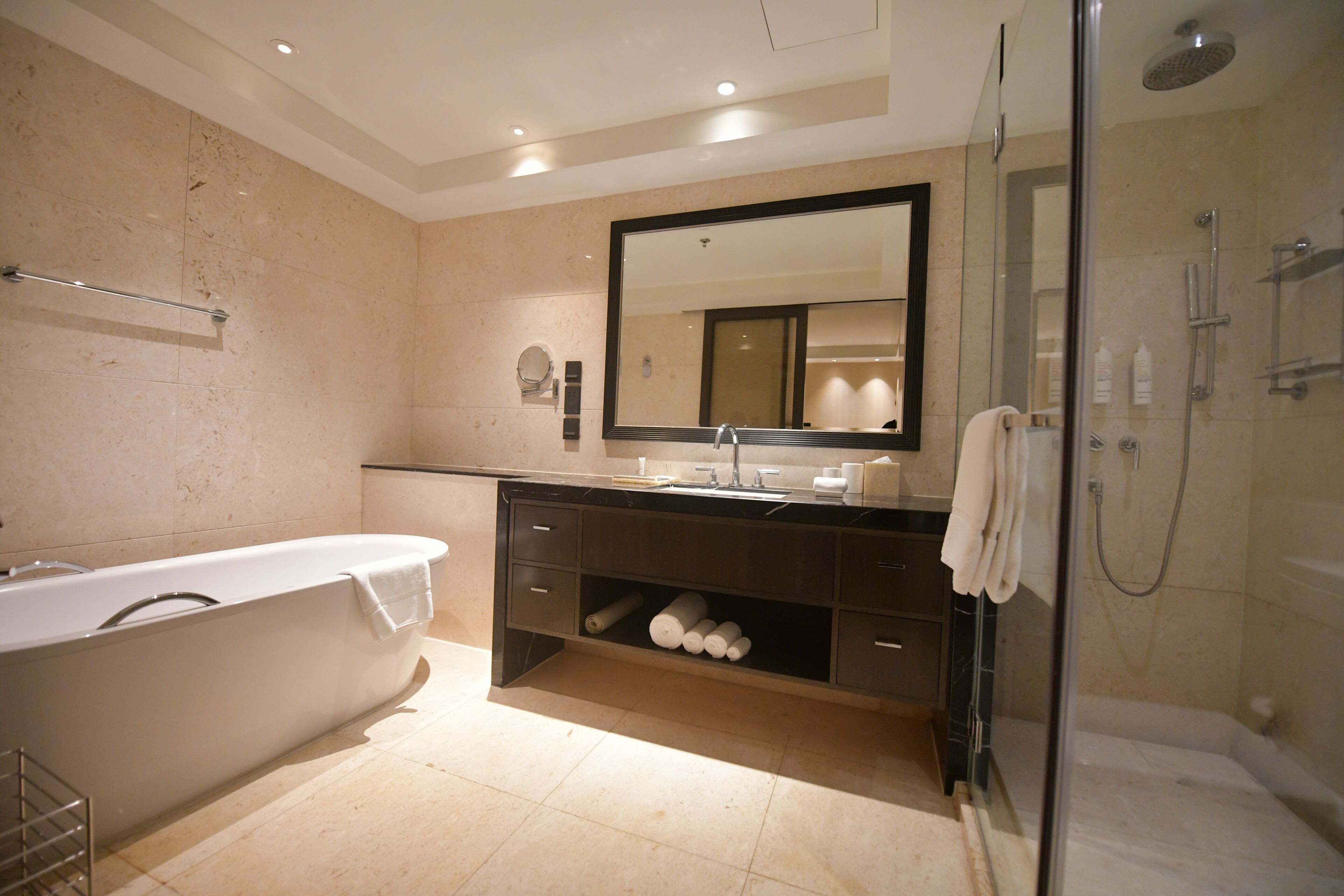 A modern bathroom with a freestanding bathtub, a large mirror, a glass-enclosed shower, and a vanity with storage.
