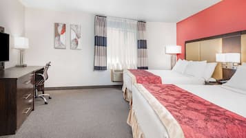 A hotel room with two beds, a desk, a TV, and a window with curtains.