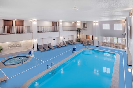 An indoor swimming pool with multiple levels, lounge chairs, and a hot tub.