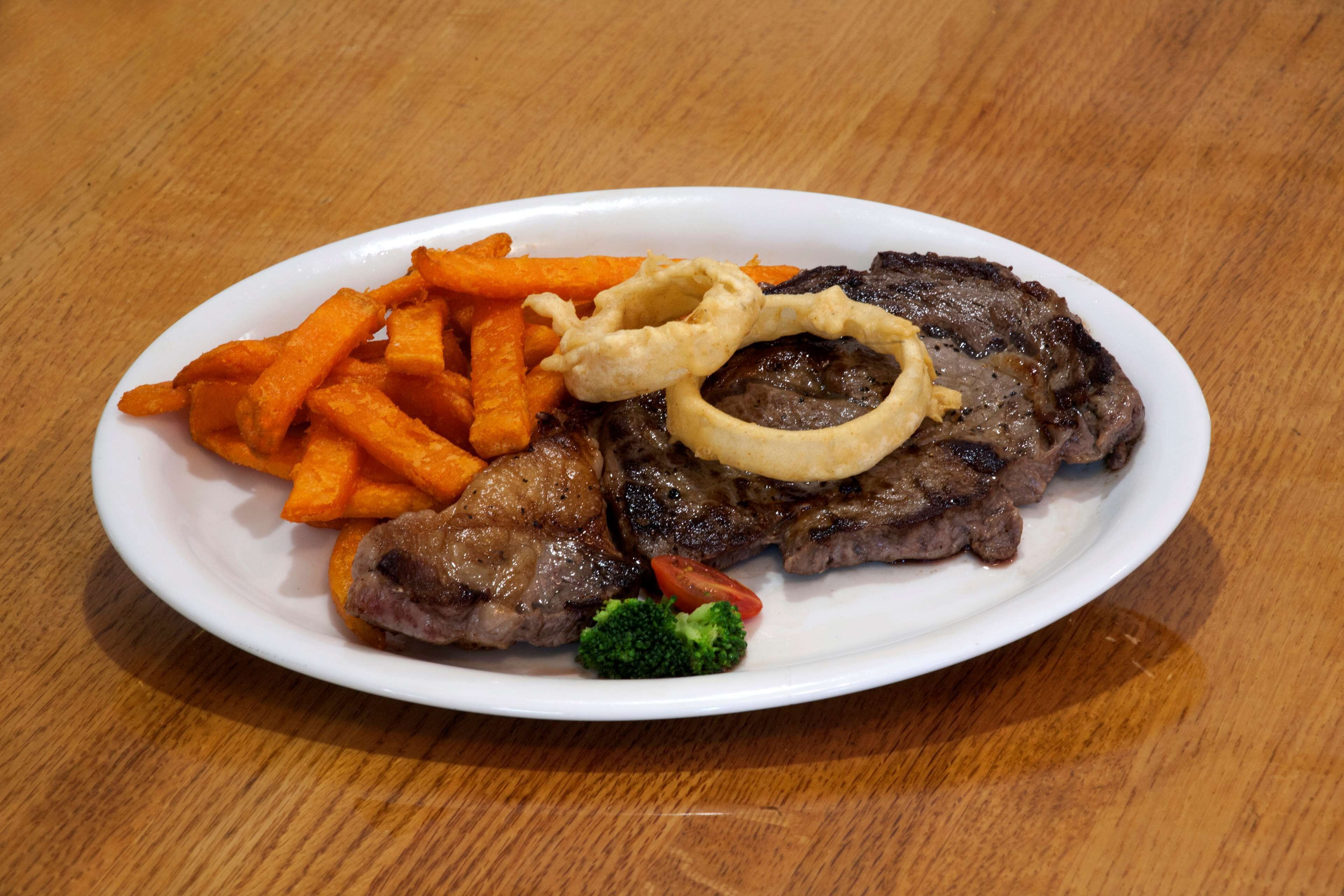 Un plato con bistec, papas fritas, cebollas en aros y brócoli.