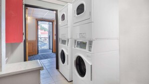 A laundry room with stacked washing machines and dryers, a red cabinet, and a tiled floor. - Ramada by Wyndham Keystone Near Mt Rushmore (Keystone)