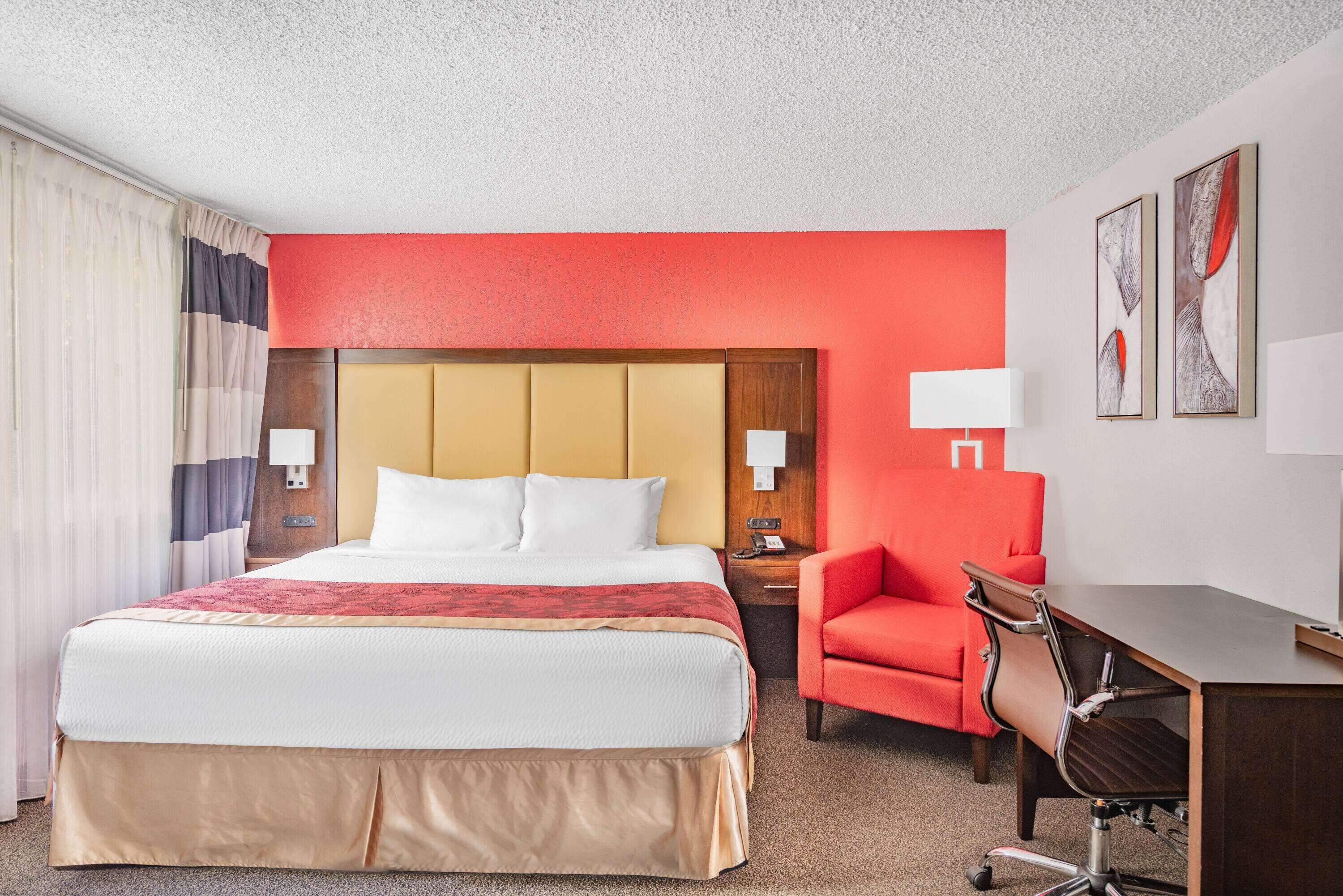 Habitación de hotel con una cama grande, un escritorio con silla, una pared de acento roja y dos lámparas de pared.