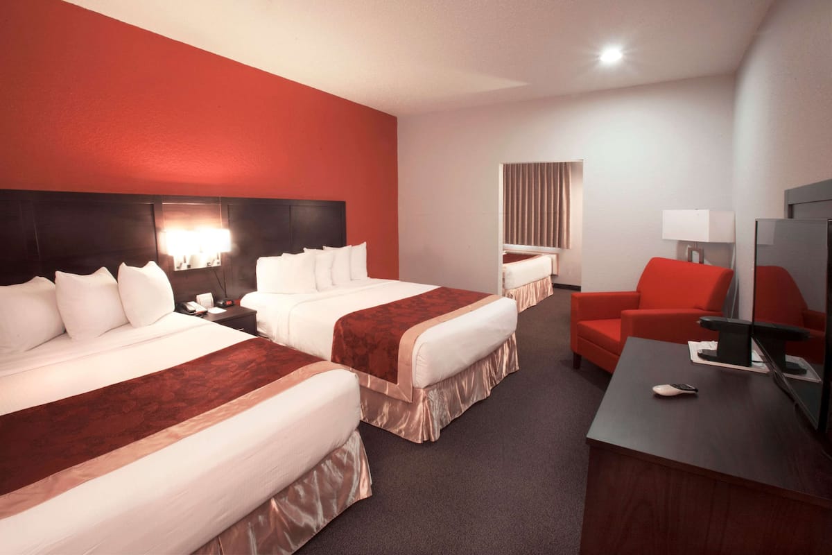 A hotel room with two beds, a desk, a chair, a TV, and a lamp.