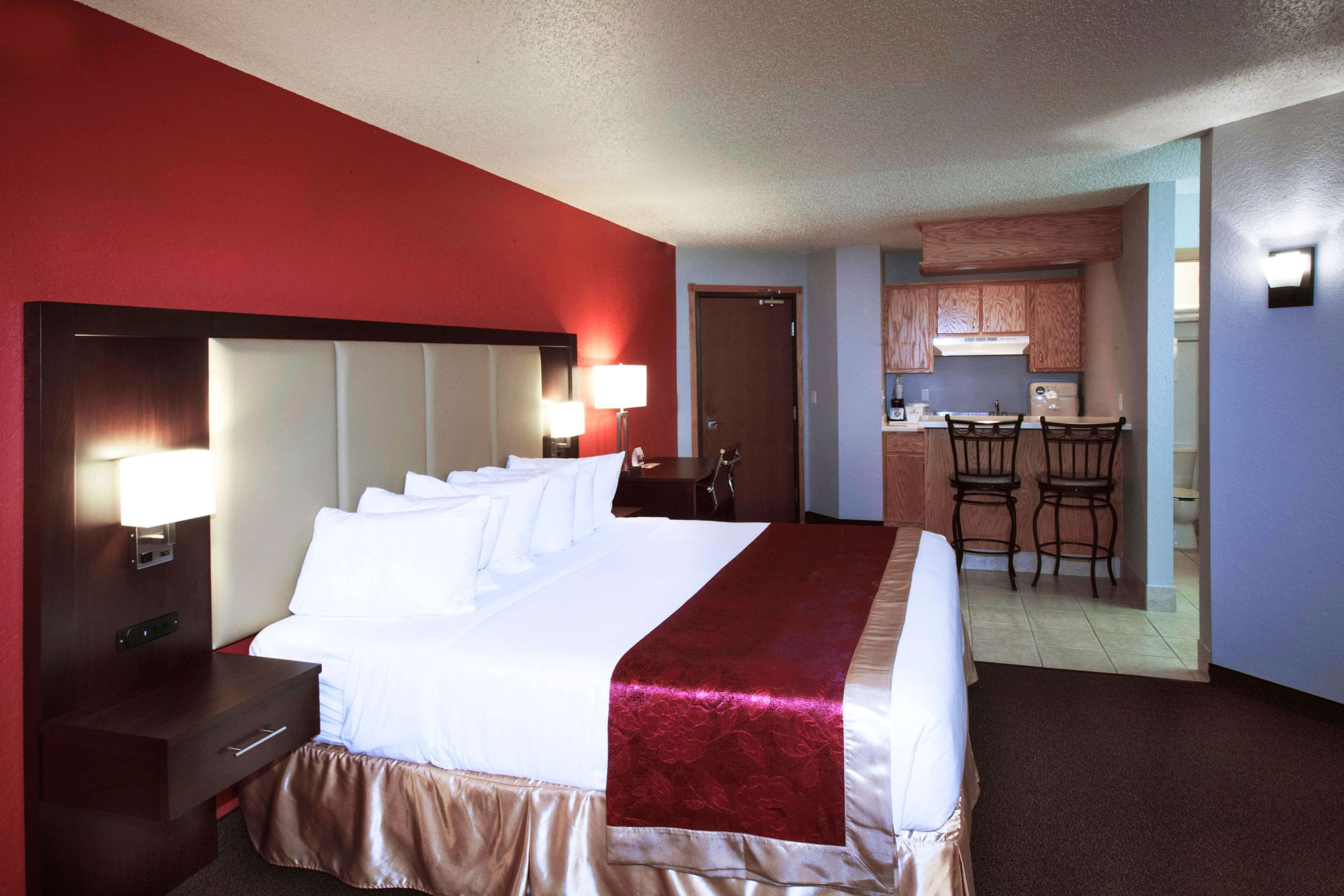 A hotel room with a large bed, a nightstand, a desk, and a kitchenette.