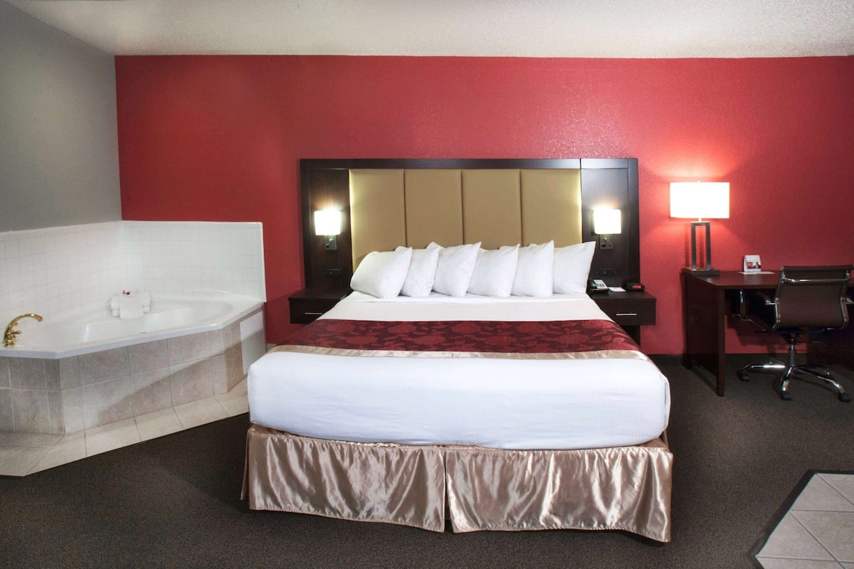 A hotel room with a large bed, a separate bathroom with a bathtub, a desk, and a chair.