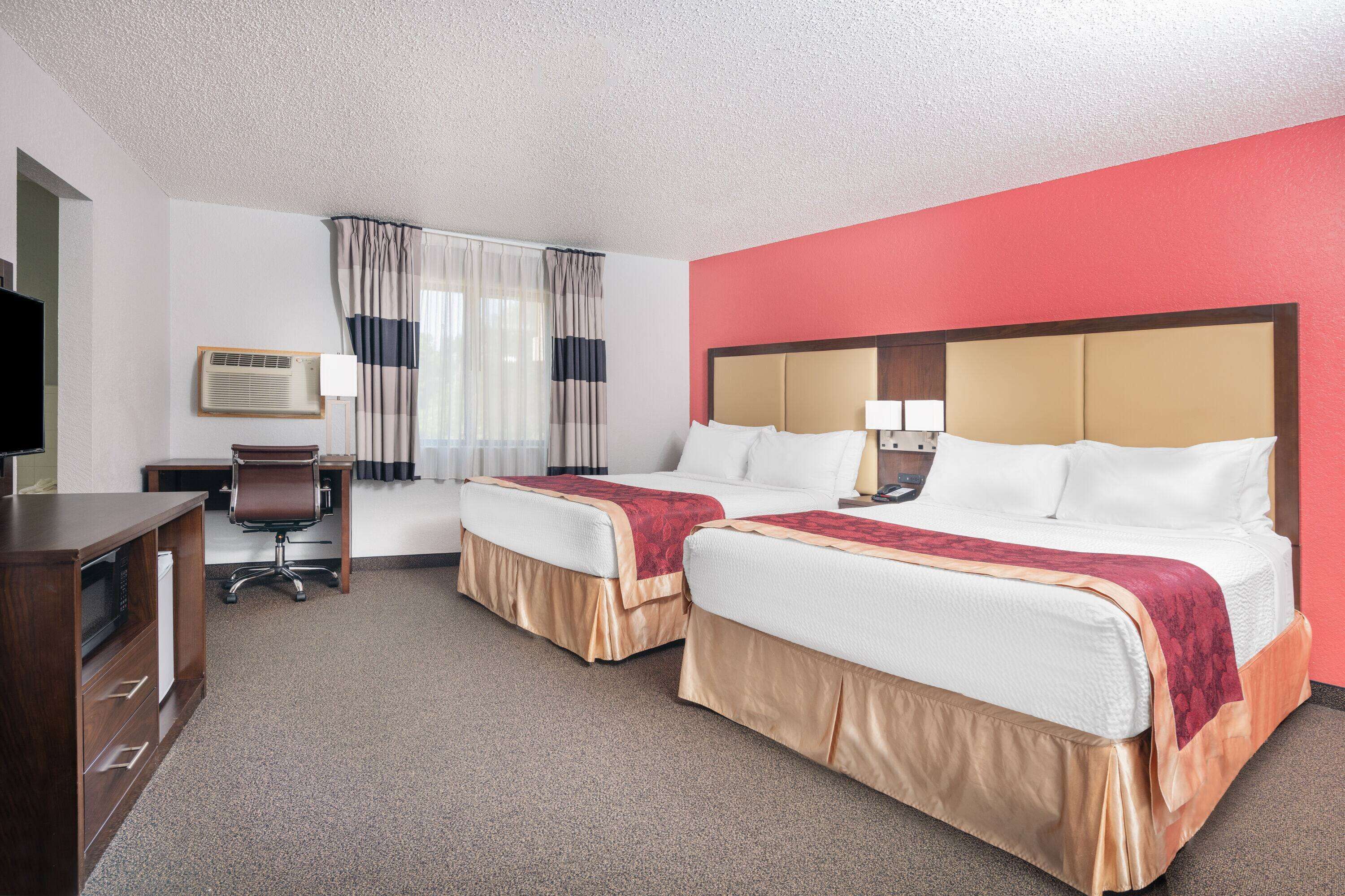 A hotel room with two beds, a desk, a chair, a television, and a window with curtains.
