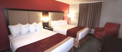 A hotel room with two beds, a red wall, a red armchair, and a lamp.
