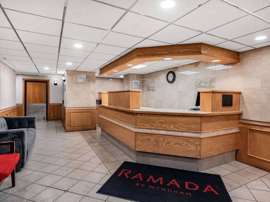 A reception area with a wooden reception desk, a clock on the wall, and a doormat with "RAMADA" written on it.