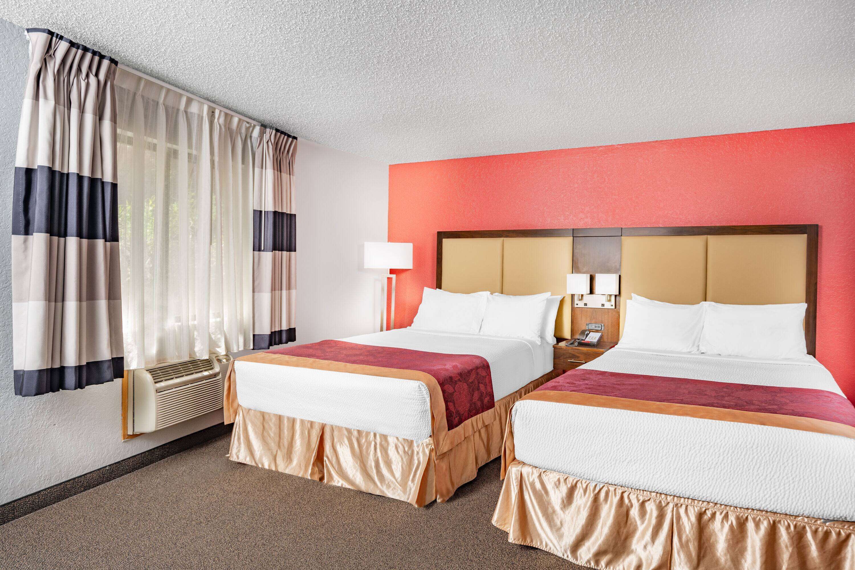 Una habitación de hotel con dos camas, una pared decorada en rojo y un ventanal con cortinas.
