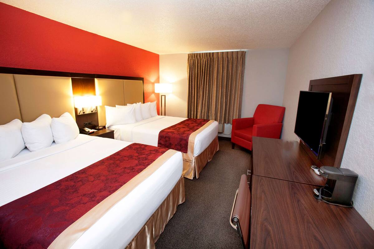 A hotel room with two beds, a TV, a desk, and a red chair.