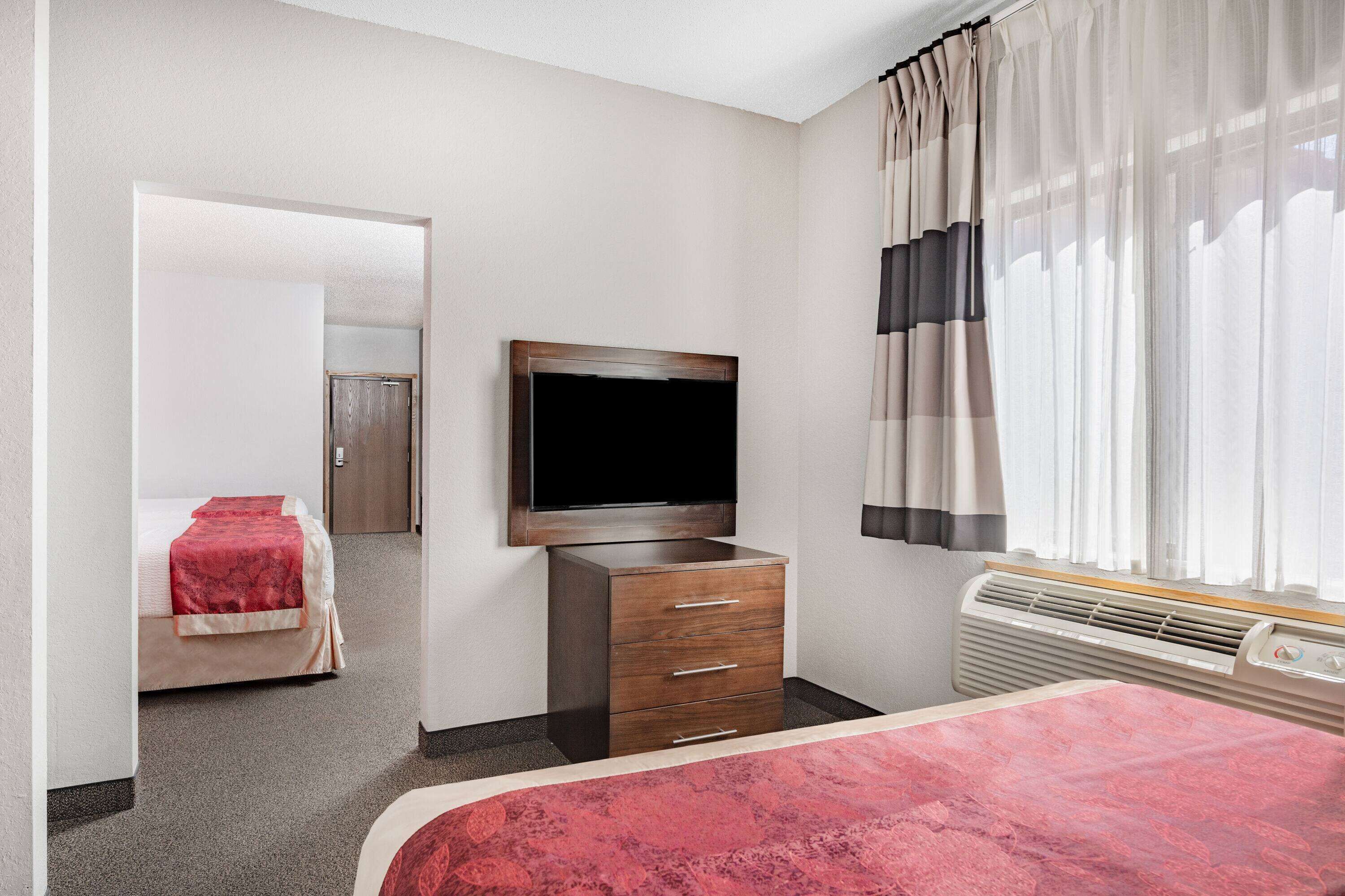 A hotel room with a bed, a TV mounted on the wall, a dresser, and a window with curtains.