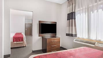 A hotel room with a bed, a TV mounted on the wall, a dresser, and a window with curtains.