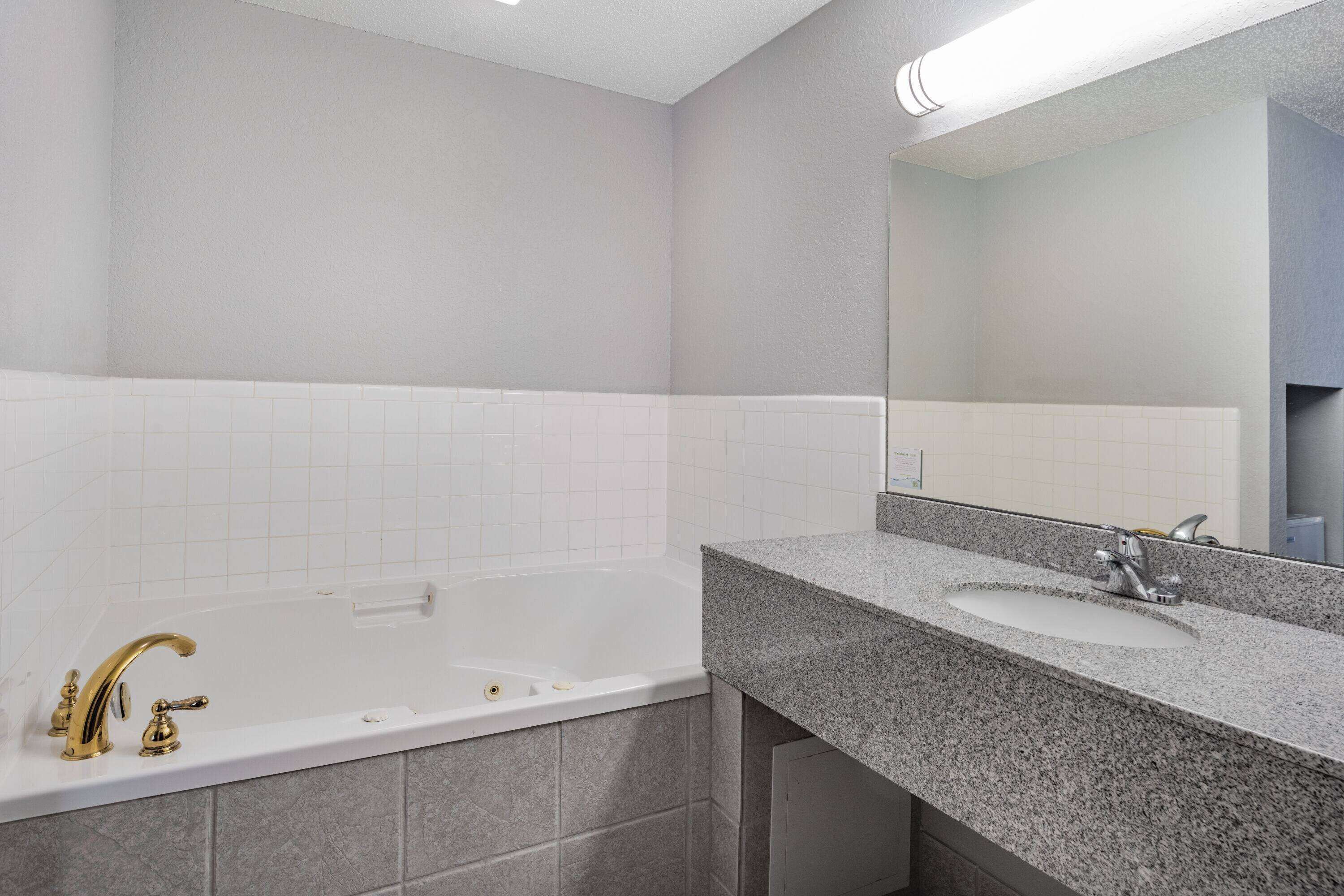 A modern bathroom with a white bathtub, a granite countertop sink, and a large mirror above the sink.