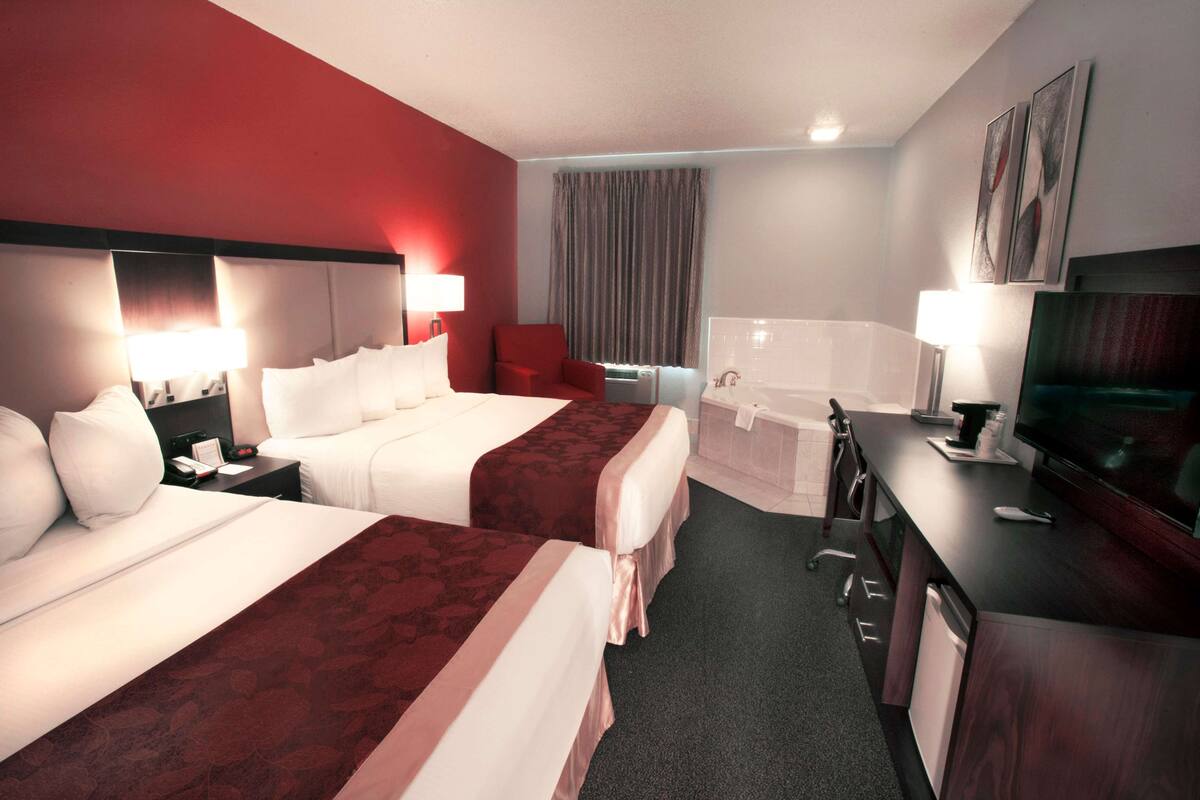 A hotel room with two beds, a desk, a television, and a bathroom.