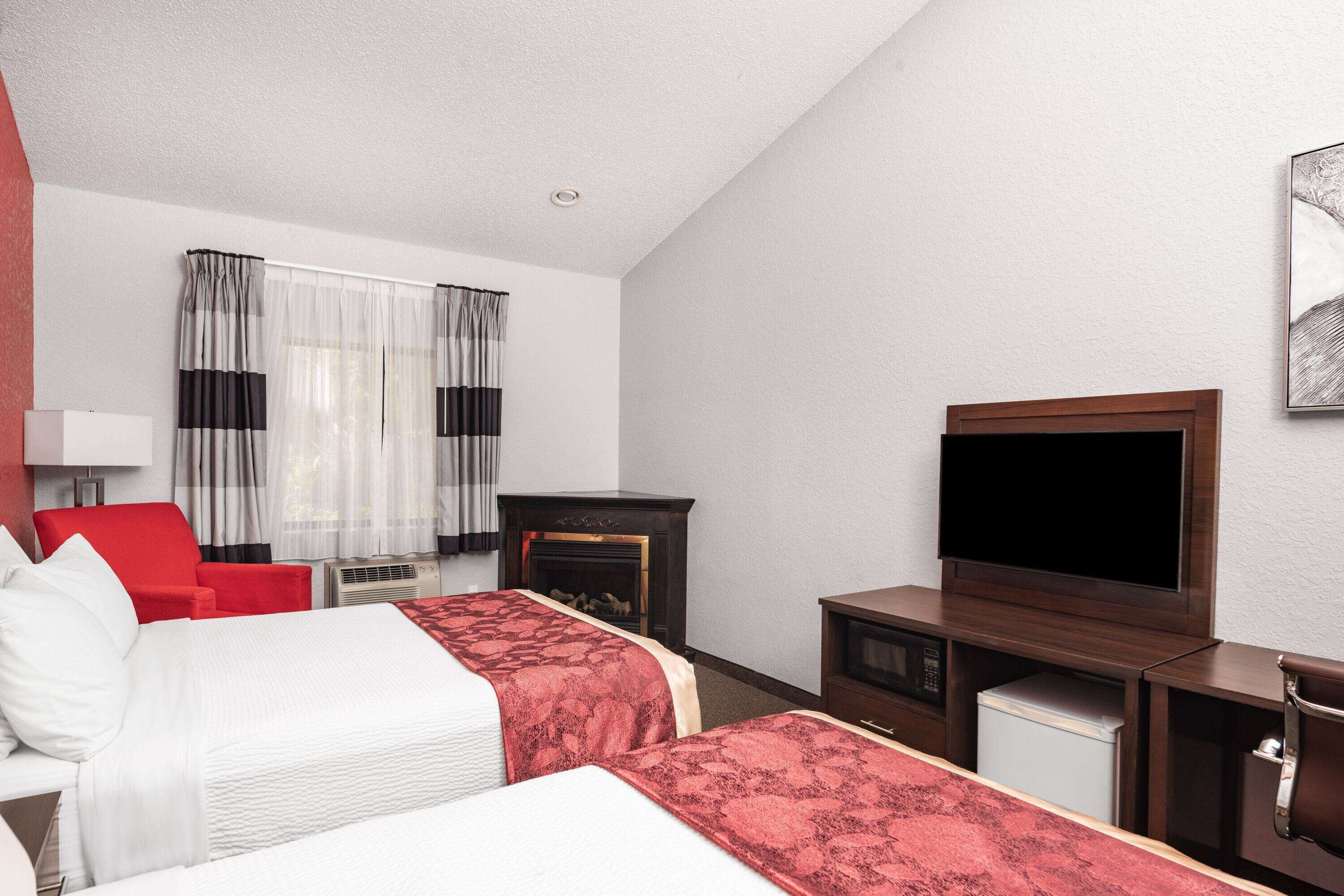 A hotel room with two beds, a TV, a fireplace, and a desk with a microwave.