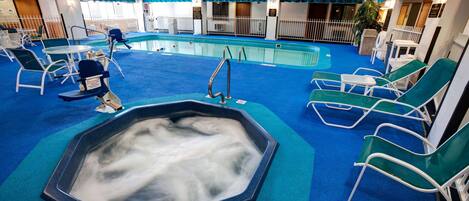 An indoor swimming pool with lounge chairs and a hot tub.