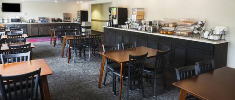 A hotel dining area with multiple tables and chairs, a kitchen counter with various appliances, and a buffet setup.