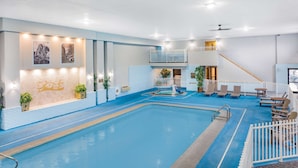 An indoor swimming pool with a blue floor, surrounded by white railings and seating areas. - Baymont by Wyndham Keystone Near Mt. Rushmore (Keystone)