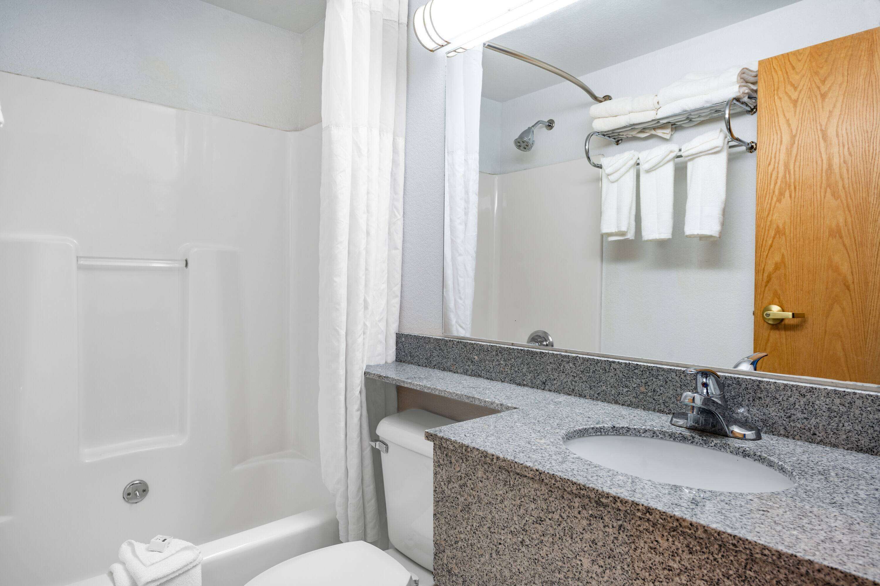 A bathroom with a shower, toilet, sink, and a wooden door.