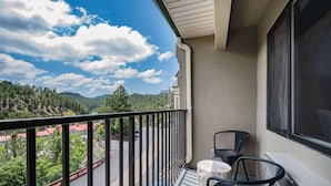 A balcony with a view of a road and trees, a railing, and two chairs. - Baymont by Wyndham Keystone Near Mt. Rushmore (Keystone)