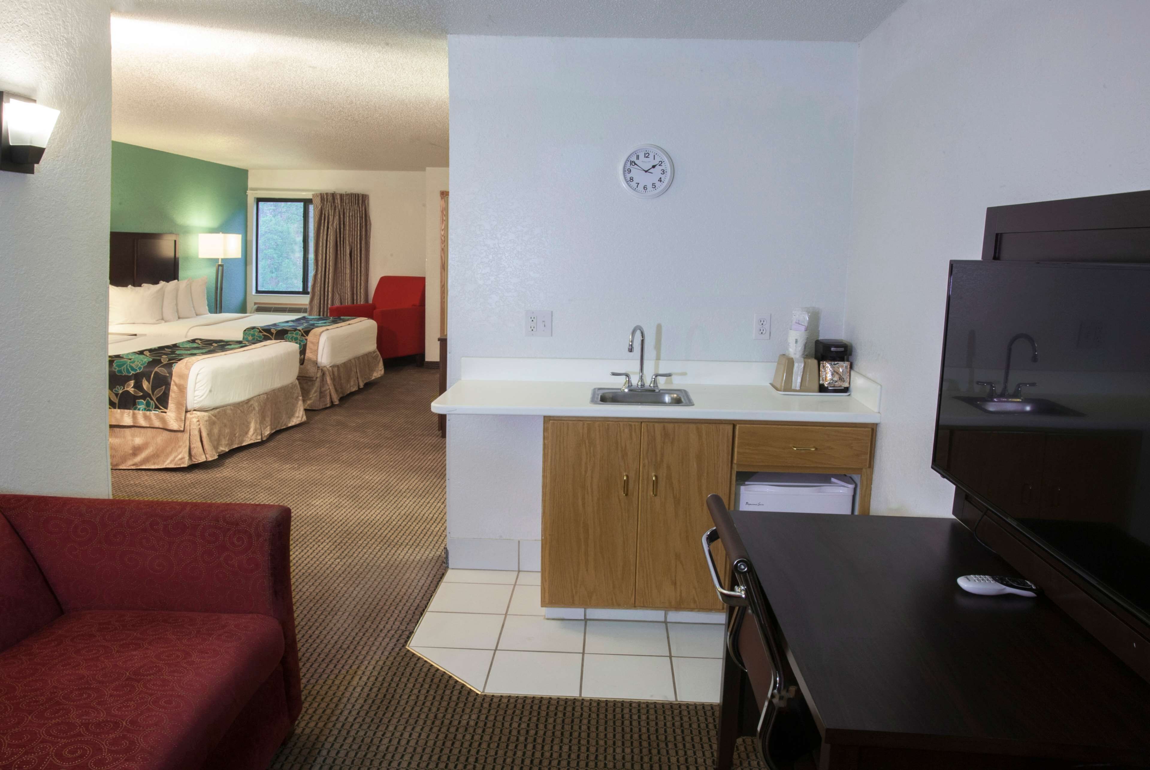 Una habitación de hotel con kitchenette, una cama, una silla roja y un televisor.