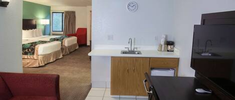 Una habitación de hotel con kitchenette, una cama, una silla roja y un televisor.