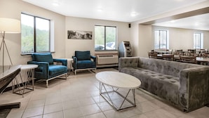 A spacious room with a grey sofa, blue armchairs, a round table, and a dining area with multiple chairs. - Baymont by Wyndham Keystone Near Mt. Rushmore (Keystone)