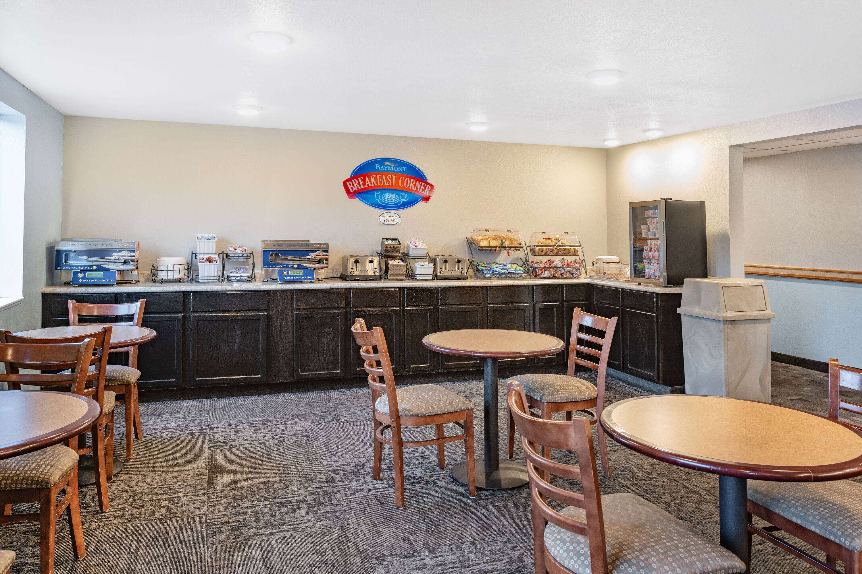 A breakfast area with wooden tables and chairs, a coffee station, and a sign reading "Breakfast Corner".