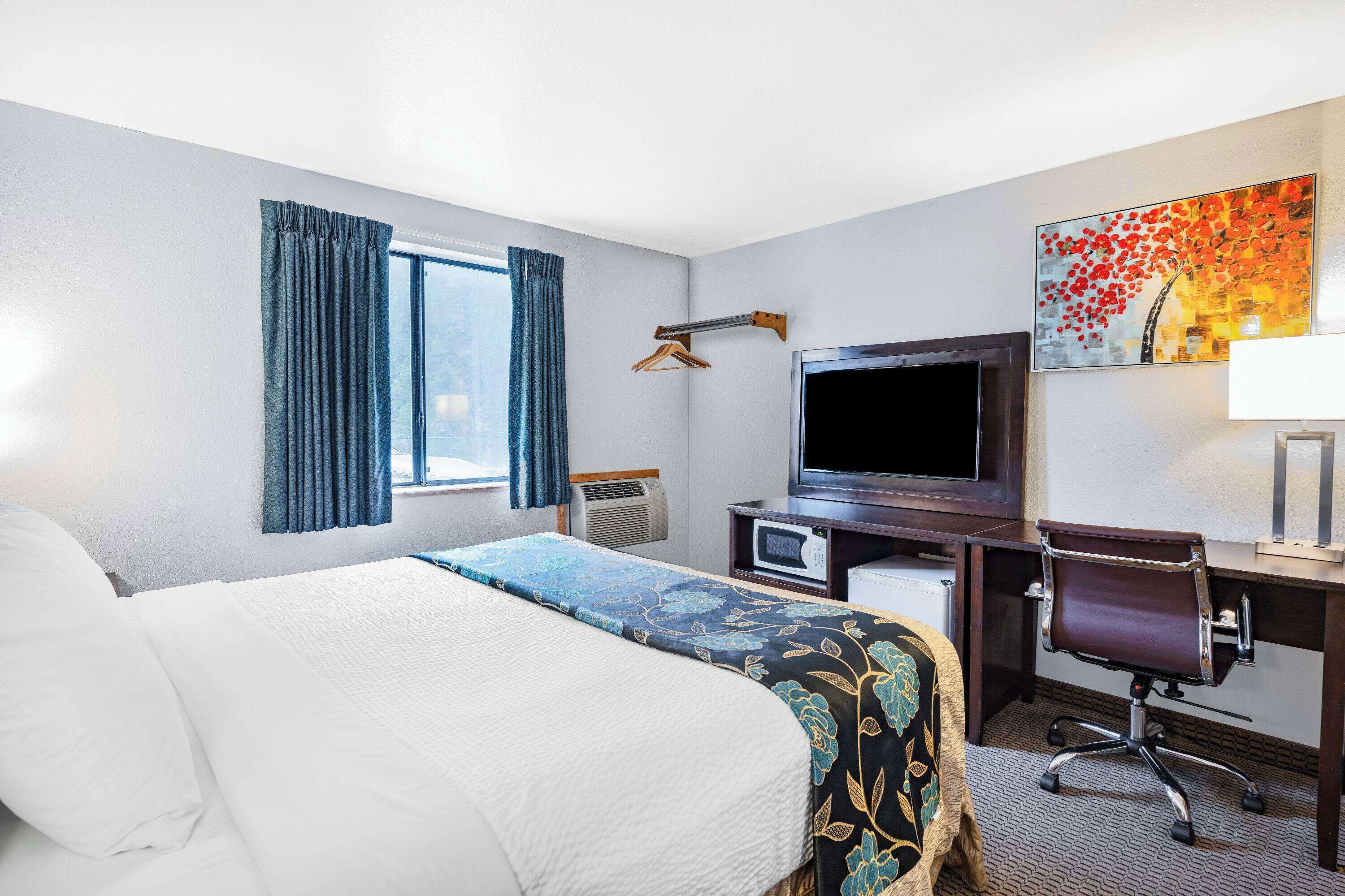 A hotel room with a bed, a desk with a computer, a TV, and a painting on the wall.