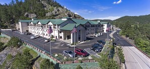 A multi-story hotel with a green roof, parking lot, and American flags. - Baymont by Wyndham Keystone Near Mt. Rushmore (Keystone)