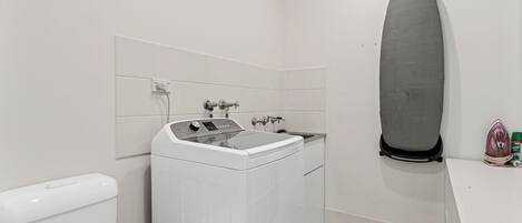 A compact bathroom with a washing machine, a toilet, and a shower area.