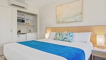 Quarto de hotel com cama, mesa de cabeceira, escrivaninha, cozinha compacta e um quadro na parede.