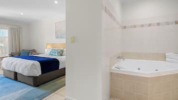 A hotel room with a bed, a blue rug, a bathroom with a bathtub, and a window with curtains.