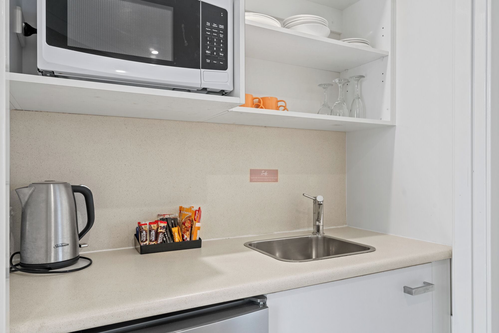 A kitchen with a microwave, a kettle, a sink, and a spice rack.
