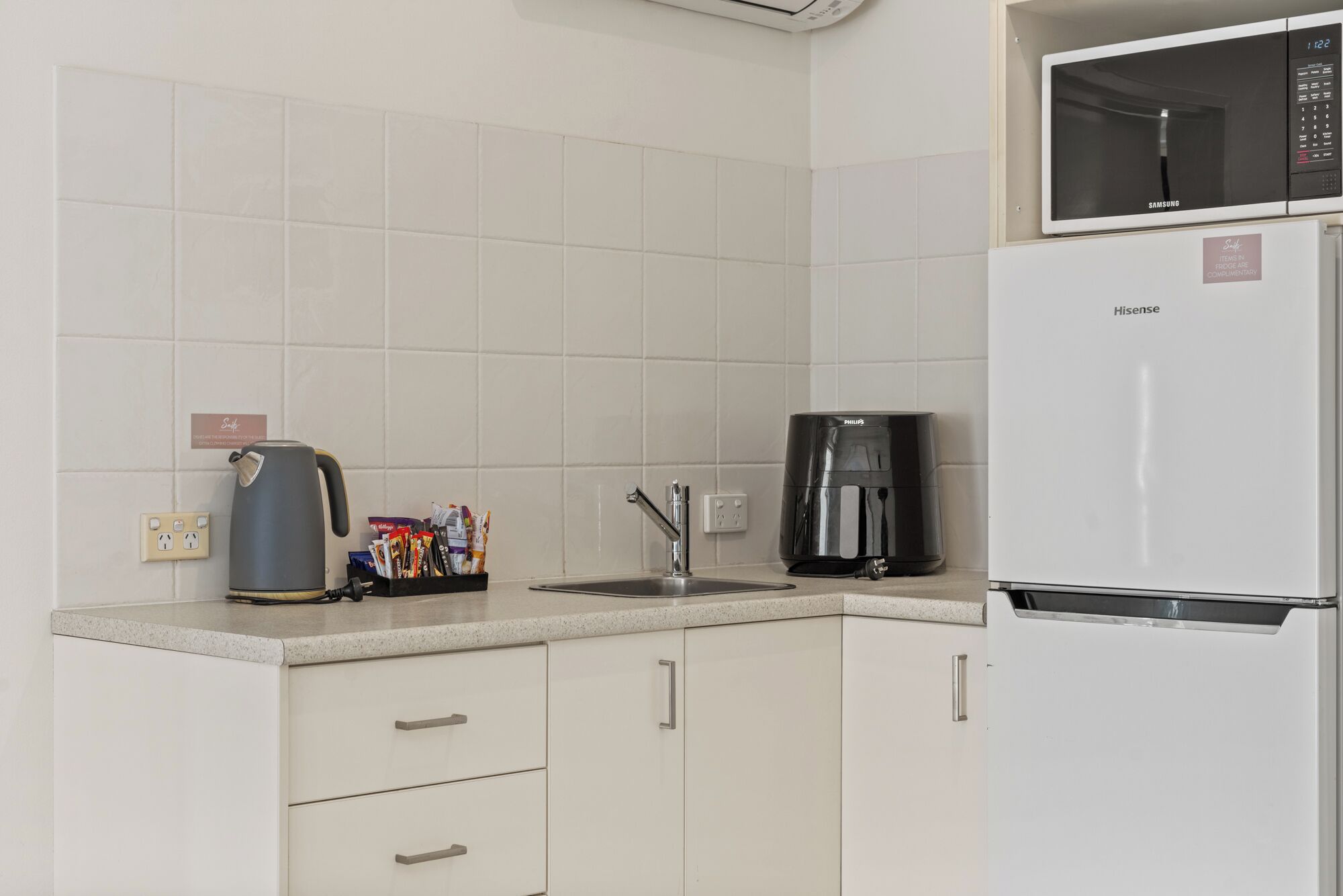 Eine moderne Küche mit weißen Schränken, einer Kaffeemaschine, einem Wasserkocher und einem Kühlschrank.