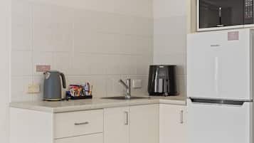 A modern kitchen with white cabinets, a coffee maker, a kettle, and a refrigerator.