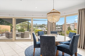 A dining area with a round table, six chairs, and a chandelier. - Terrigal Sails Serviced Apartments (Terrigal)