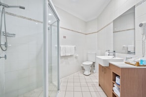 A modern bathroom with a glass shower enclosure, a toilet, and a sink with a wooden vanity. - Terrigal Sails Serviced Apartments (Terrigal)