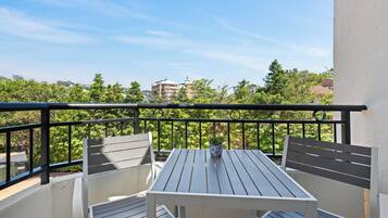 Un balcón con una mesa, dos sillas, una planta en maceta y vistas a edificios y árboles.