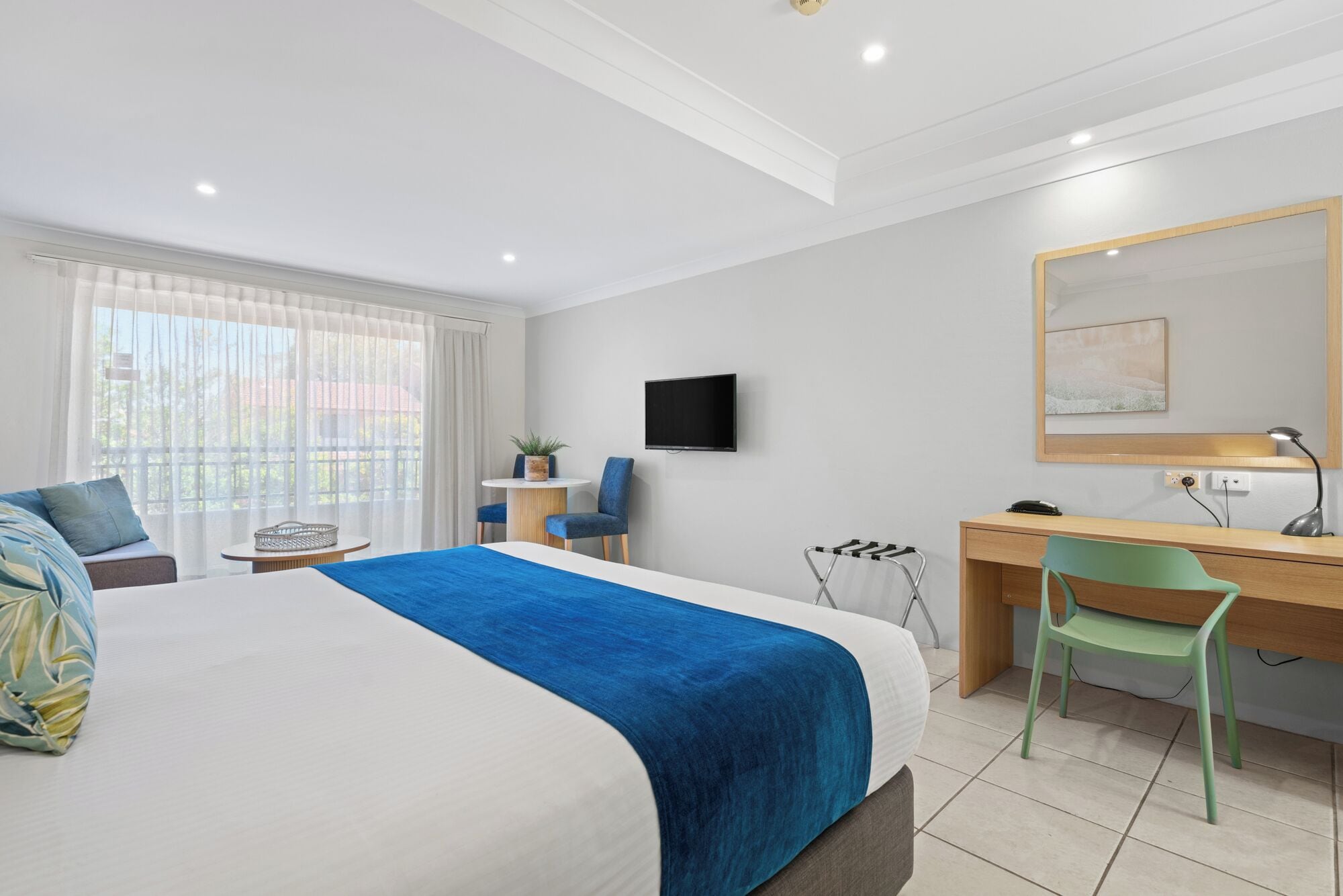 Een moderne hotelkamer met een groot bed, een bureau met stoel, een televisie en een raam met gordijnen.