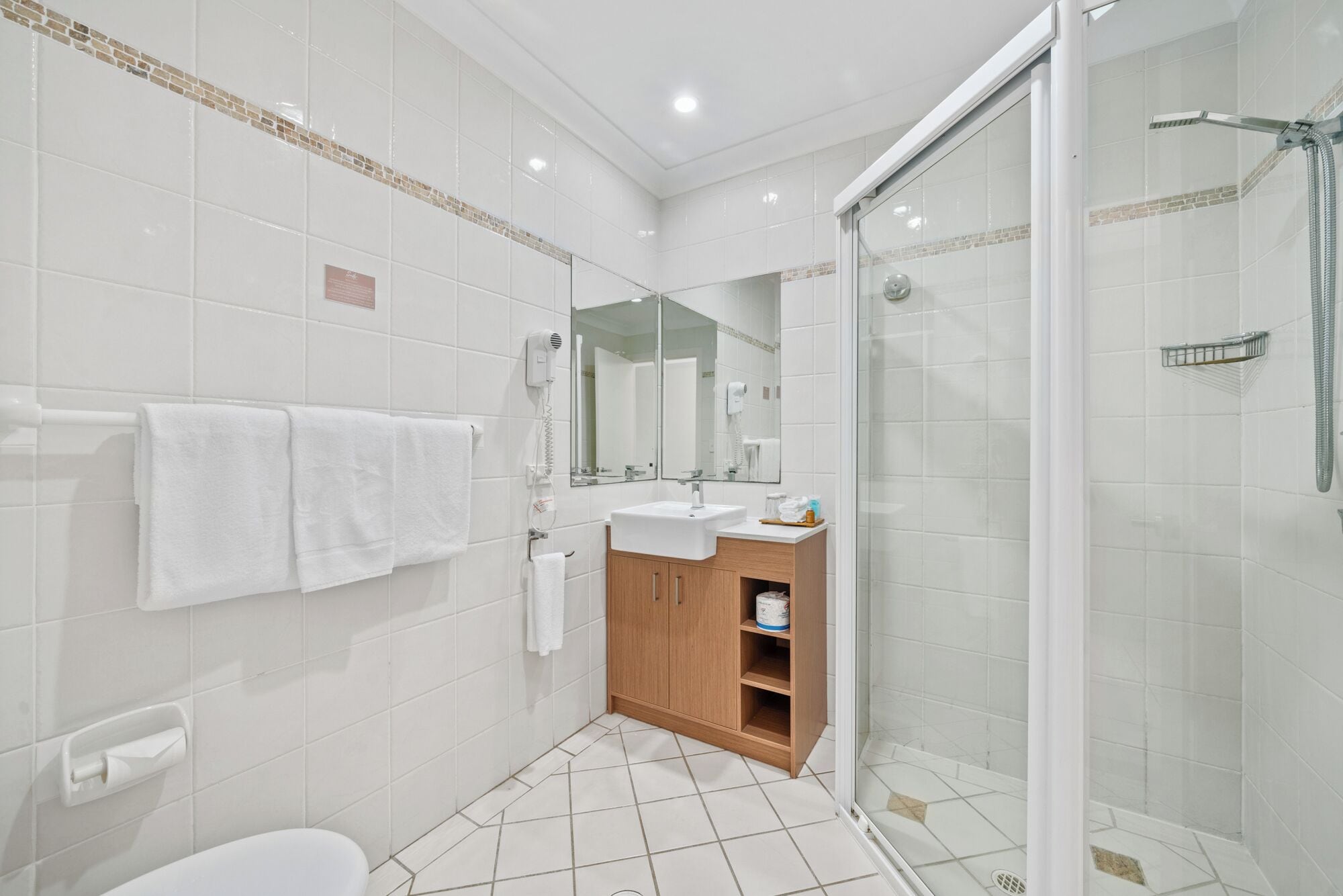 A modern bathroom with a glass shower enclosure, a white sink, and a wooden cabinet.