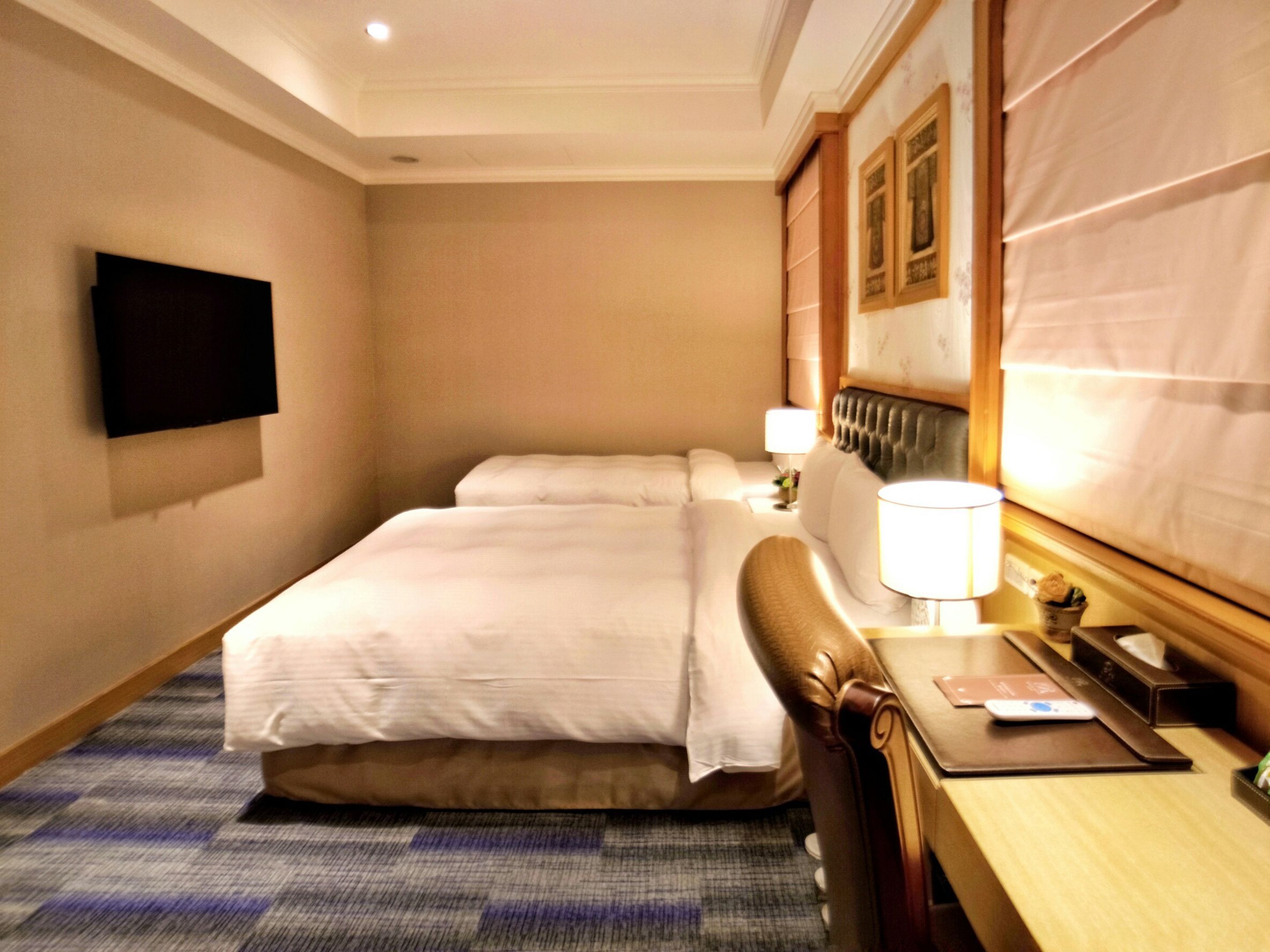 Hotelkamer met een groot bed, bureau met lamp, flatscreen-tv aan de muur en een kamerbreed tapijt met patroon.