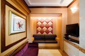 Un hall de hotel con una obra de arte enmarcada, un banco acolchado, un televisor y un panel decorativo en la pared.