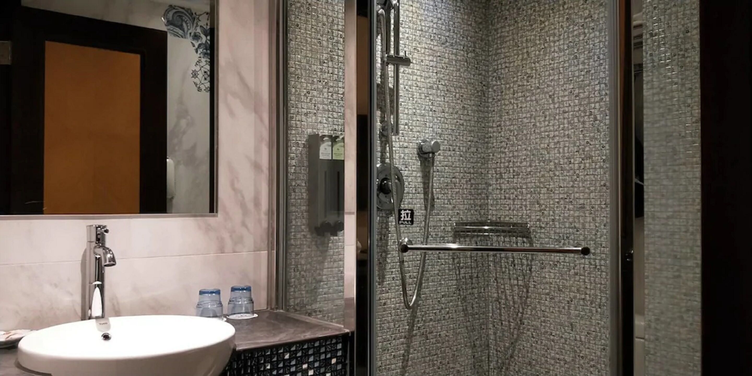 Un baño con un lavamanos blanco, un espejo y una ducha con pared texturizada.