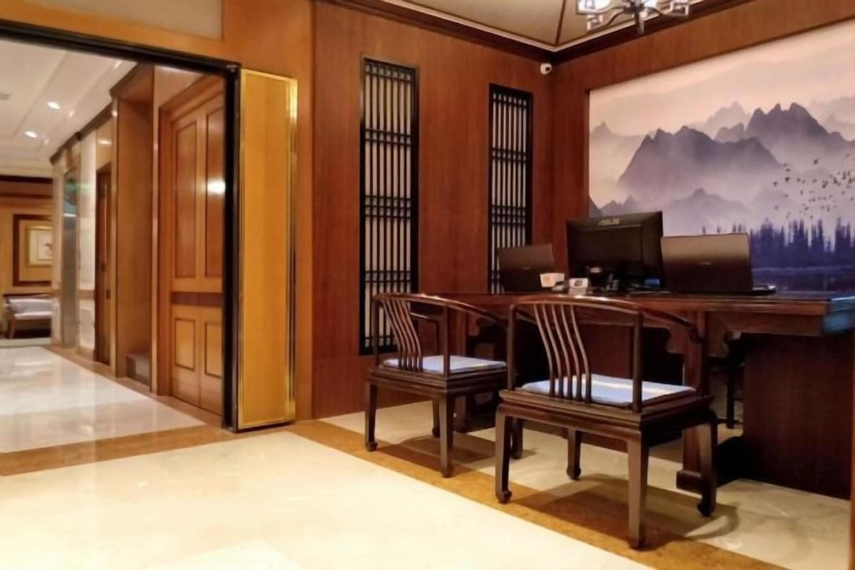 Zona de recepción de hotel con paneles de madera, dos sillas de madera, un escritorio con computadora y un gran cuadro mural de montañas.