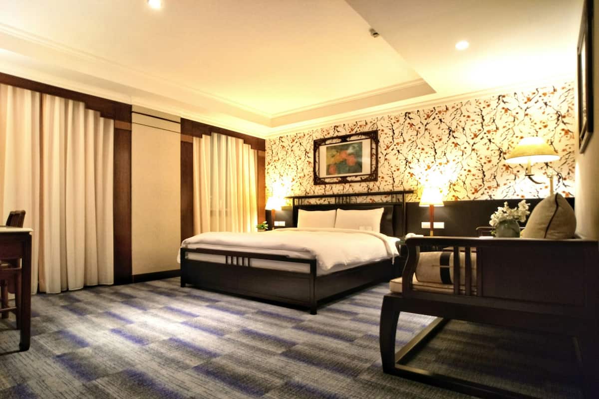 A hotel room with a large bed, a desk, a chair, and a carpeted floor.