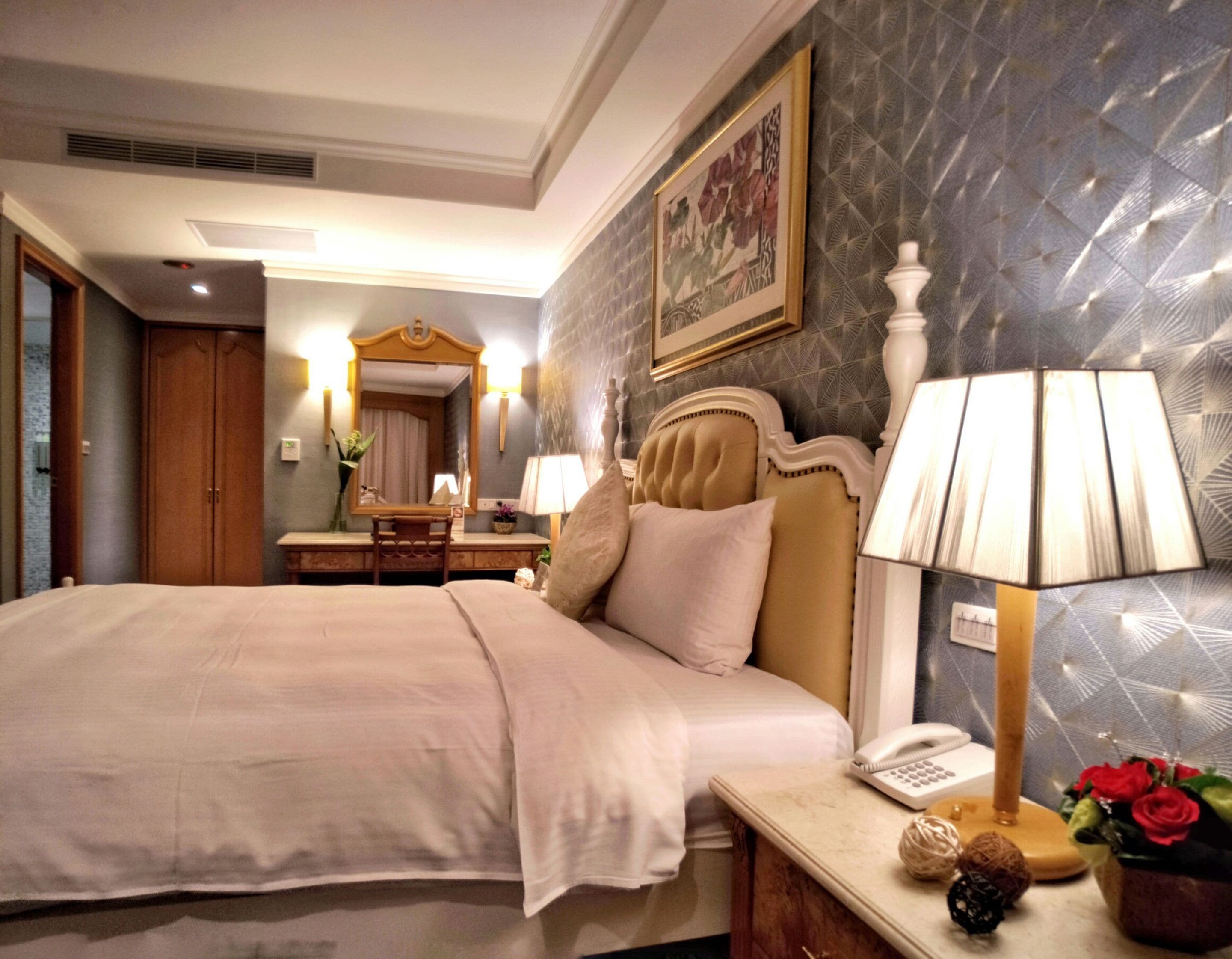 Habitación de hotel con una cama grande, una mesita de noche con lámpara, un espejo y un aparador.
