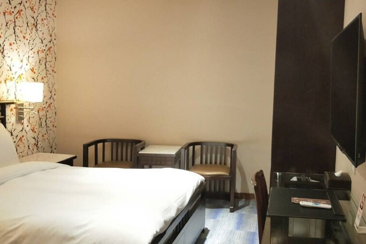A hotel room with a bed, a desk, two chairs, a television, and a wall-mounted TV.